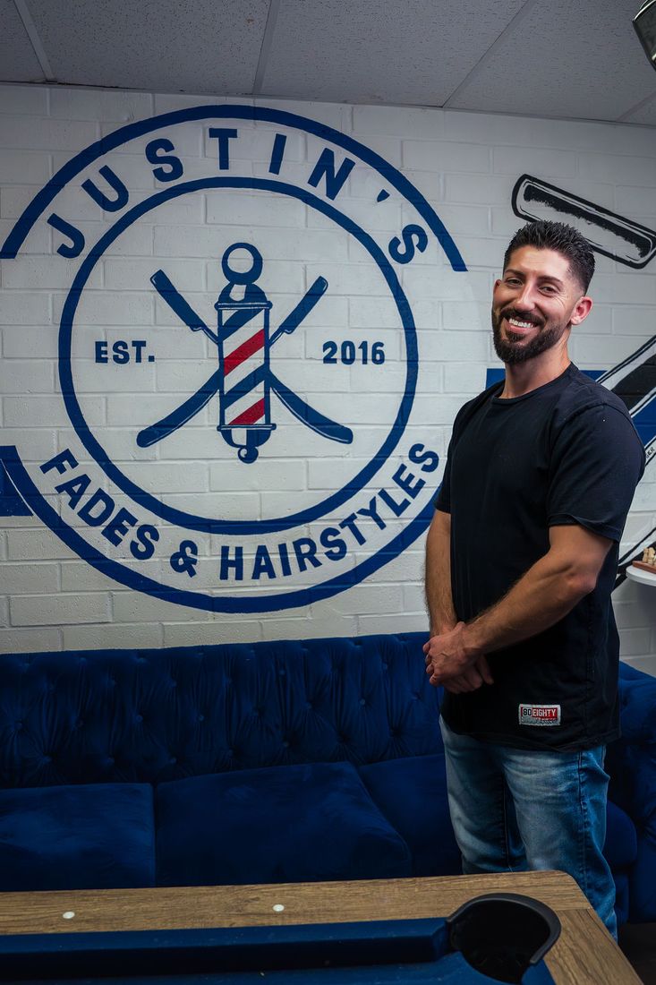 Justin Balint — owner of Justin's Fades & Hairstyles, standing by the shop's logo mural.